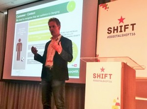 A photograph of Richard Harris from Paddy Power giving his presentation at Shift, in front of a large projector screen and a podium emblazoned with the Shift red star logo.