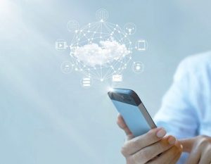 Businessman holding a smartphone, with a visual representation of cloud computing, a little white cloud connected to various icons, hovering above it.