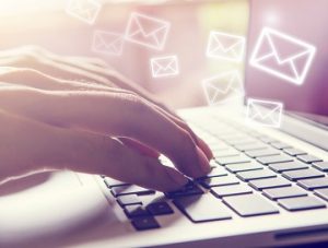 Close-up of a person's hand on a laptop keyboard, with neon closed envelope email icons floating around their fingers.